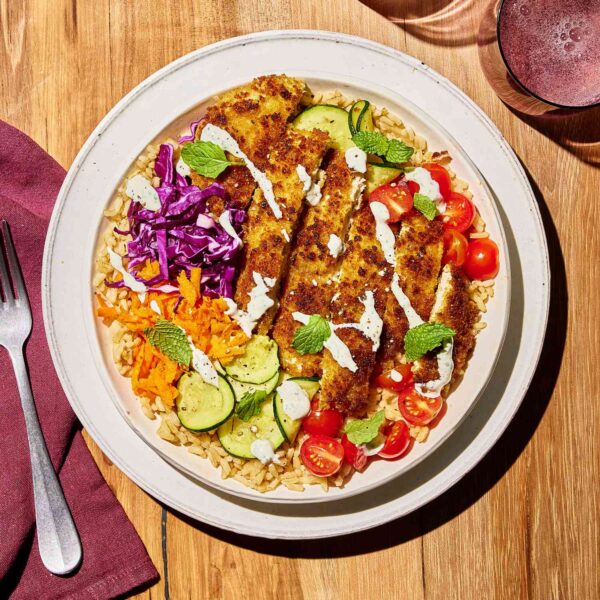 Plate of golden crispy fried chicken with garden fresh veggies like tomato, cucumber, grated carrot served with rice and dressing.